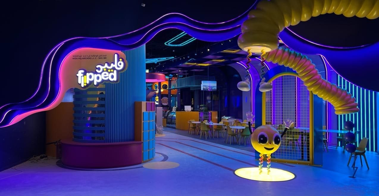 The Flipped storefront inside AA Joyland, with the glowing neon flipped wordmark sign and mascot greeting visitors at the entrance
