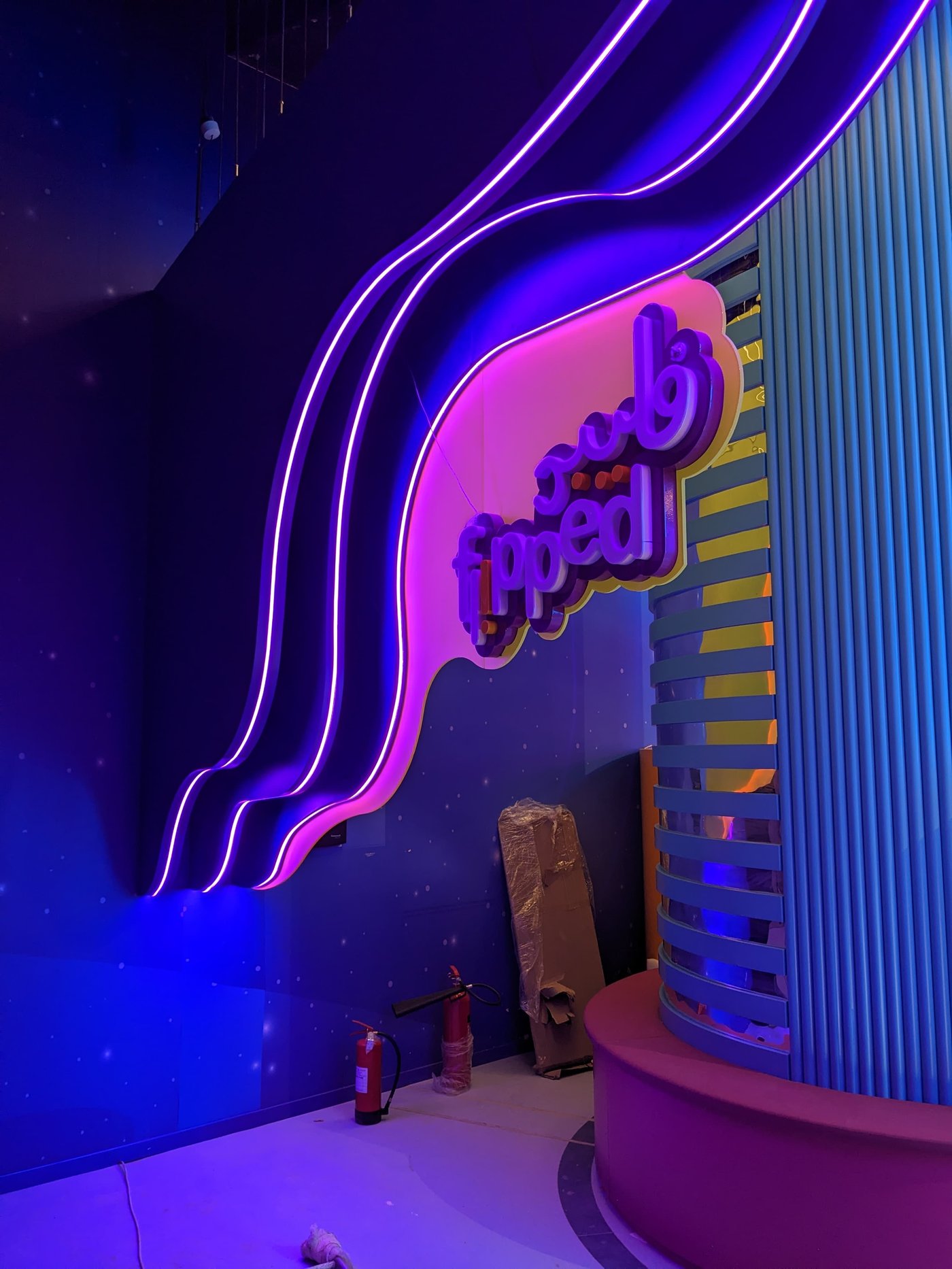 The glowing purple neon Flipped wordmark sign mounted on a tall feature wall