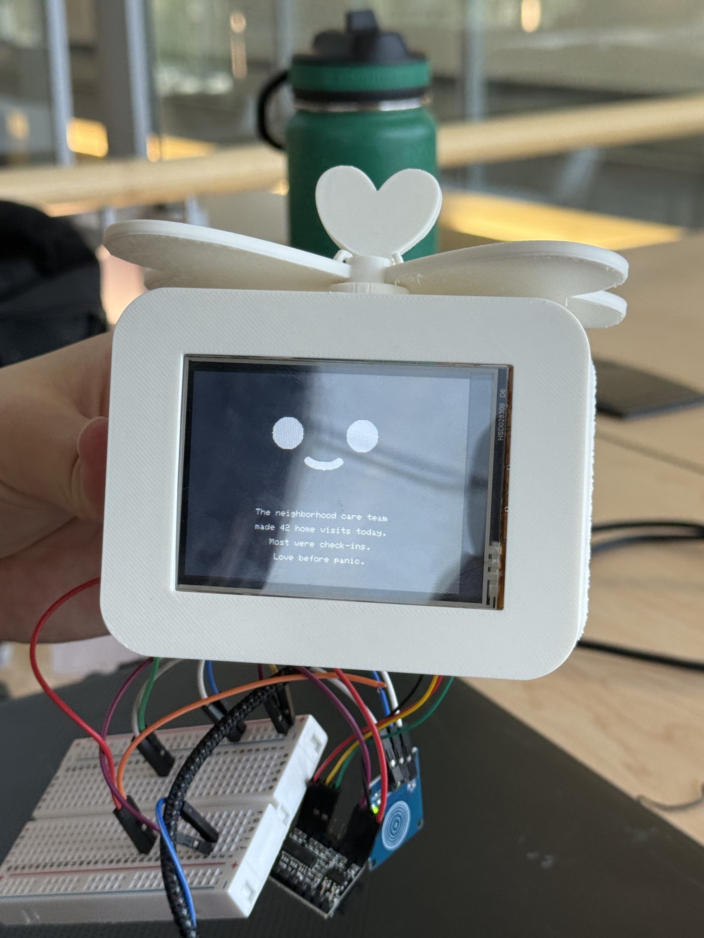 Close-up of the breadboard prototype's screen displaying the message: The neighborhood care team made 42 home visits today. Most were check-ins. Love before panic.