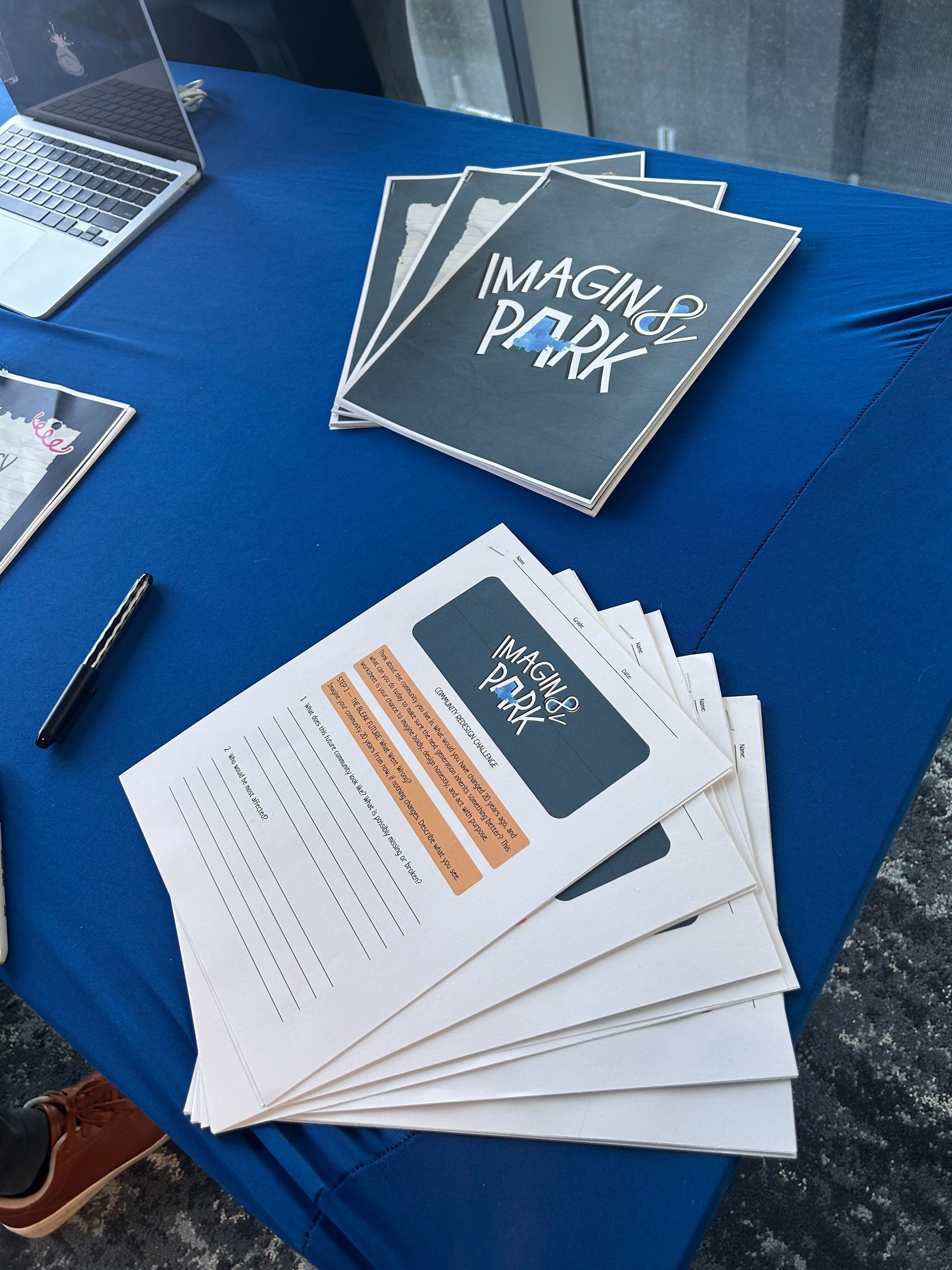 Stacks of printed Imagin8V Park Community Redesign Challenge worksheet booklets laid out on the exhibit table